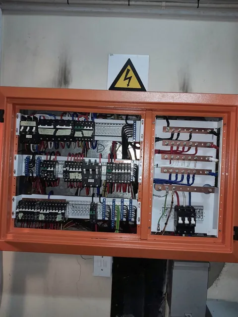 Orange two-section electrical panel with hazard sign, showing wiring and components