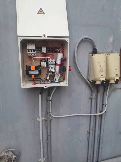 Wall-mounted control box with open lid beside two industrial sockets and conduit